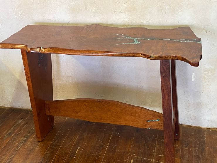 Small dark wooden table with a wavy top and two legs against a wall.