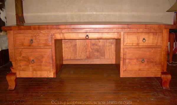Wooden desk with drawers and cabinet-style storage, shown against a beige wall on a hardwood floor.