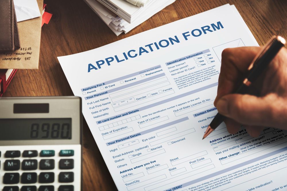 Hand filling out an application form beside a calculator on a desk