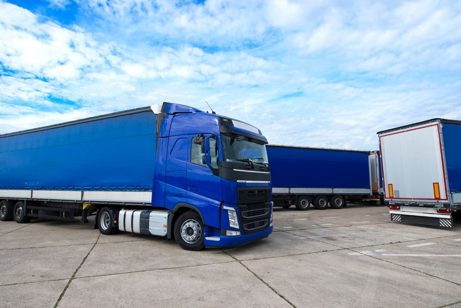 Blue semi-truck and trailer parked in a lot under a cloudy sky.