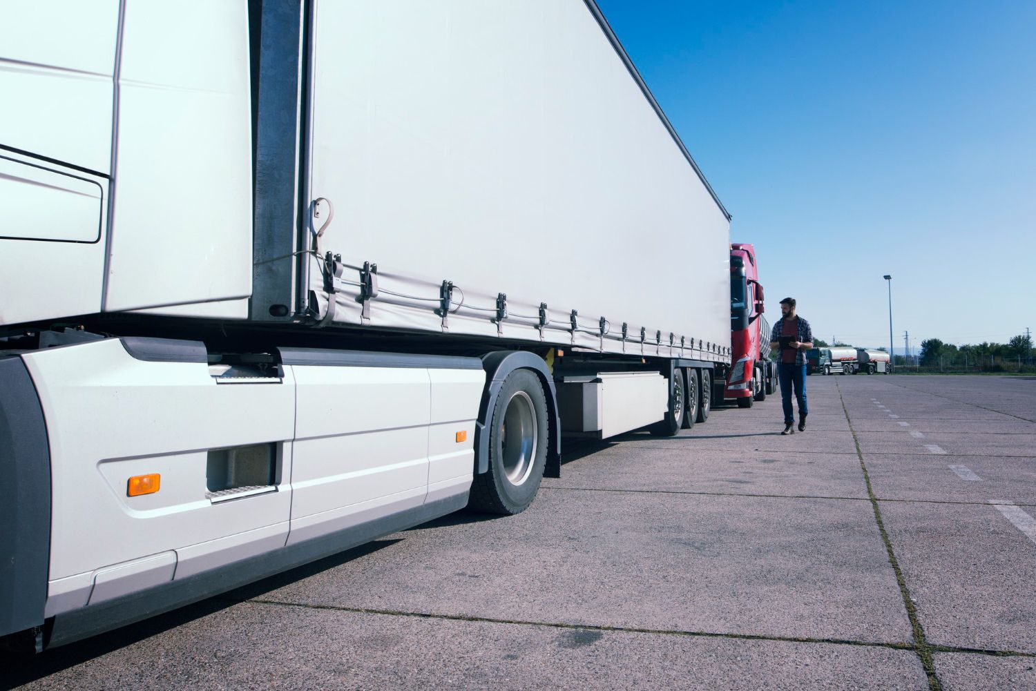 Semi-truck parked on a wide lot with a person standing near the cab under a clear blue sky