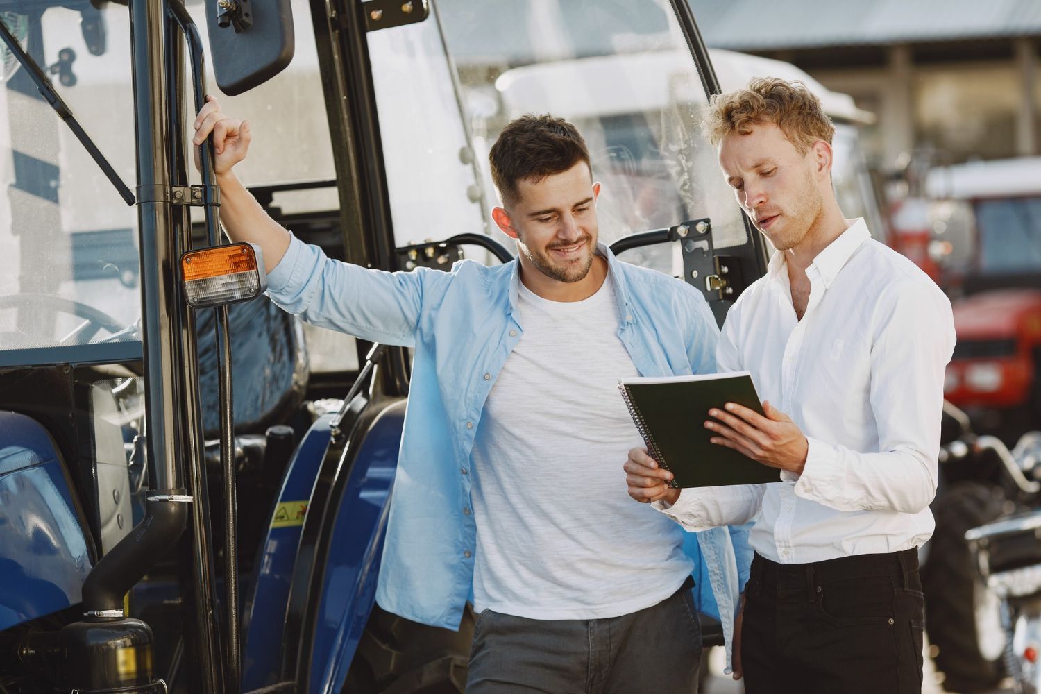 Two men standing by a bus, one holding a tablet and the other leaning on the door, discussing travel details