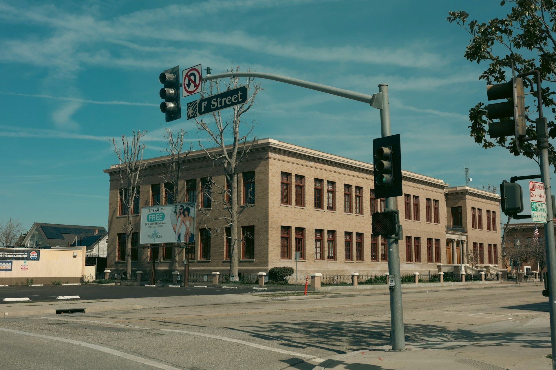 Street corner with a brick building, traffic lights, and empty intersection under a blue sky