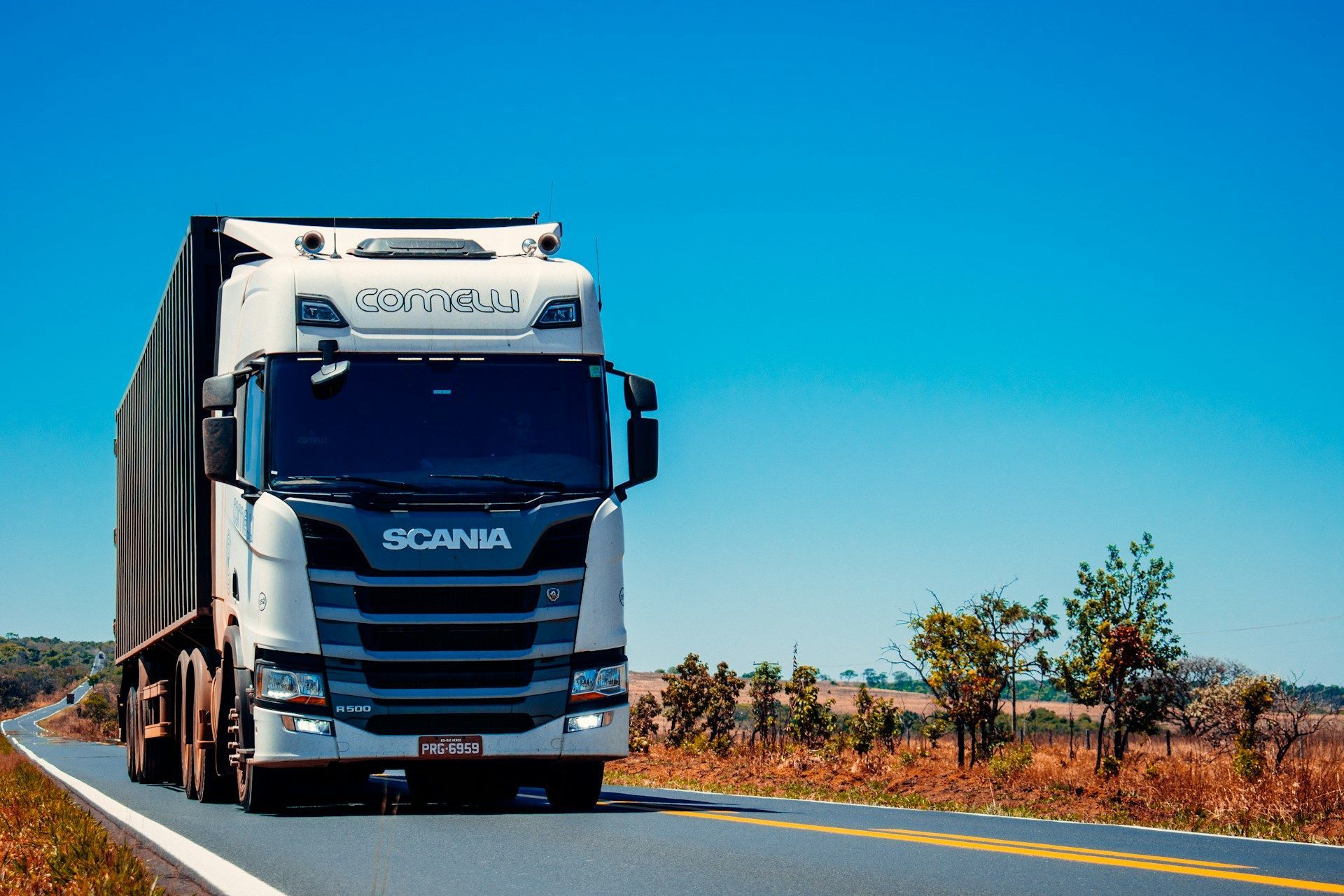 White Scania semi-truck driving on a highway under a clear blue sky