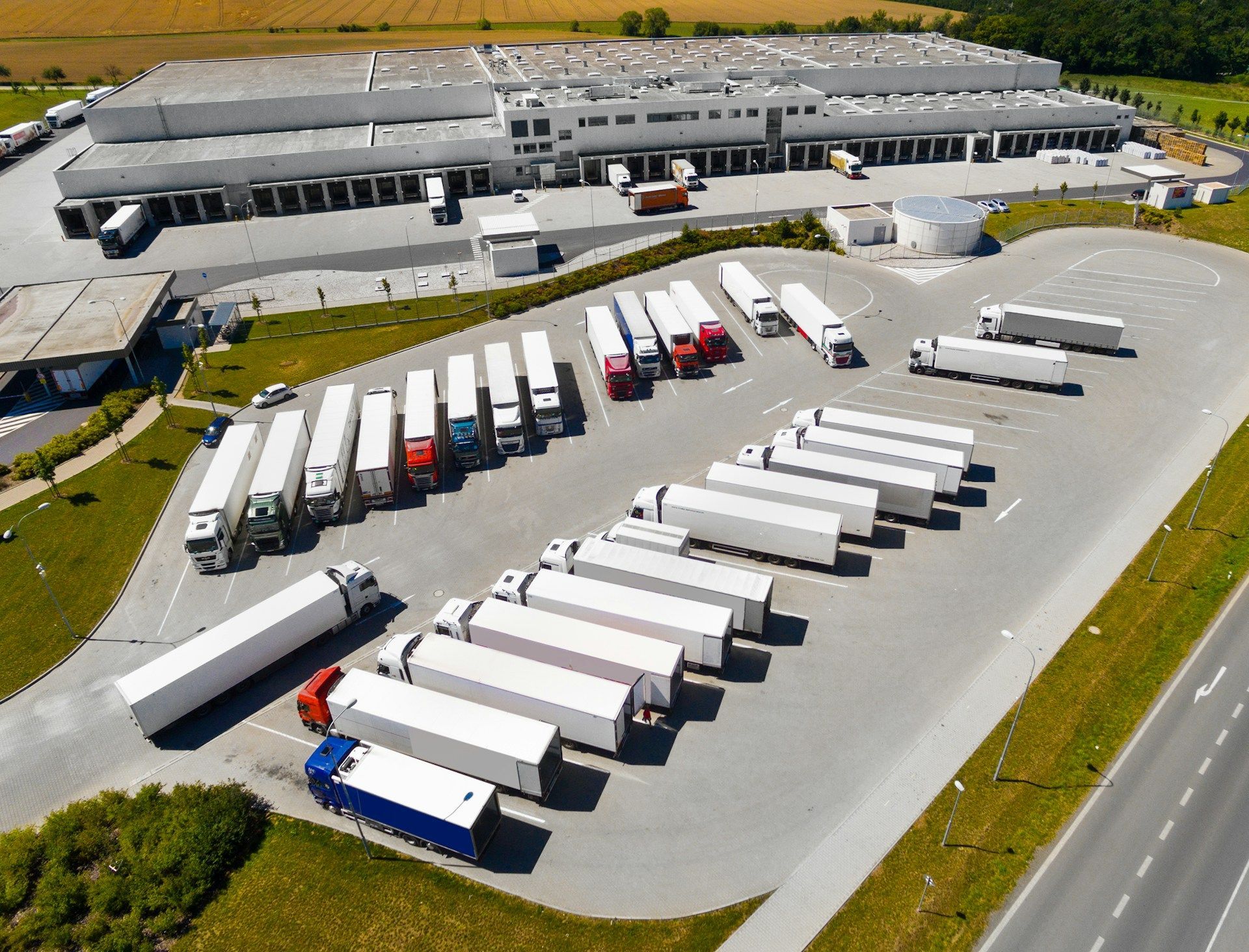Aerial view of a truck depot with rows of white trailers and a warehouse beside a road