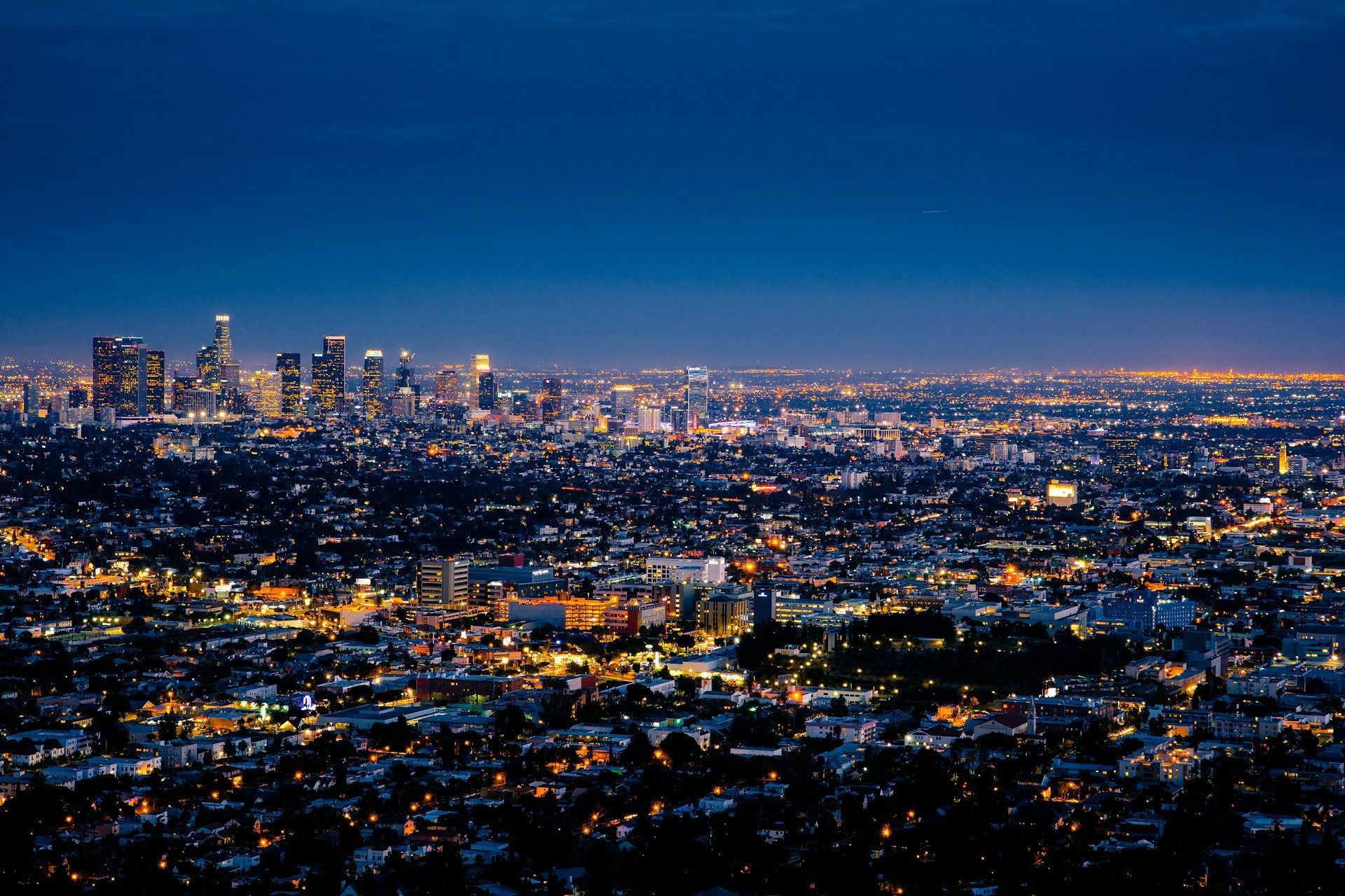 Dusk city skyline with glowing lights stretching across a vast urban landscape under a deep blue sky