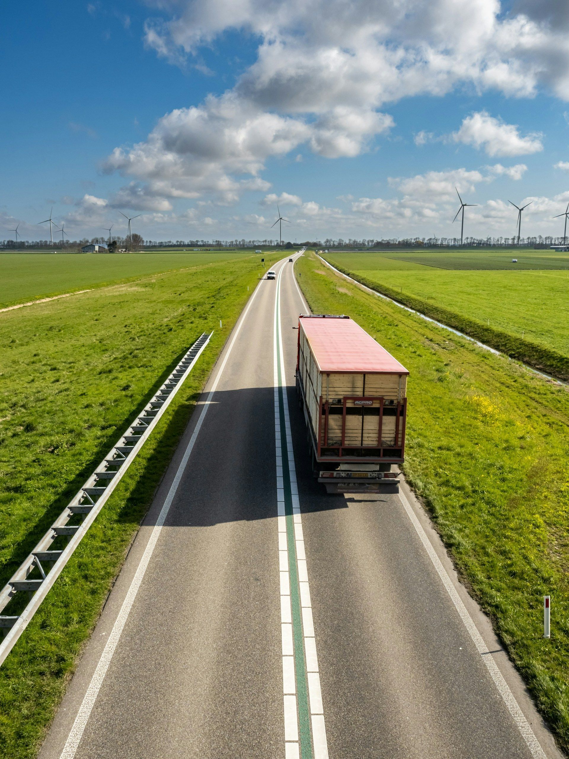 Truck driving on a rural road between green fields under a cloudy sky