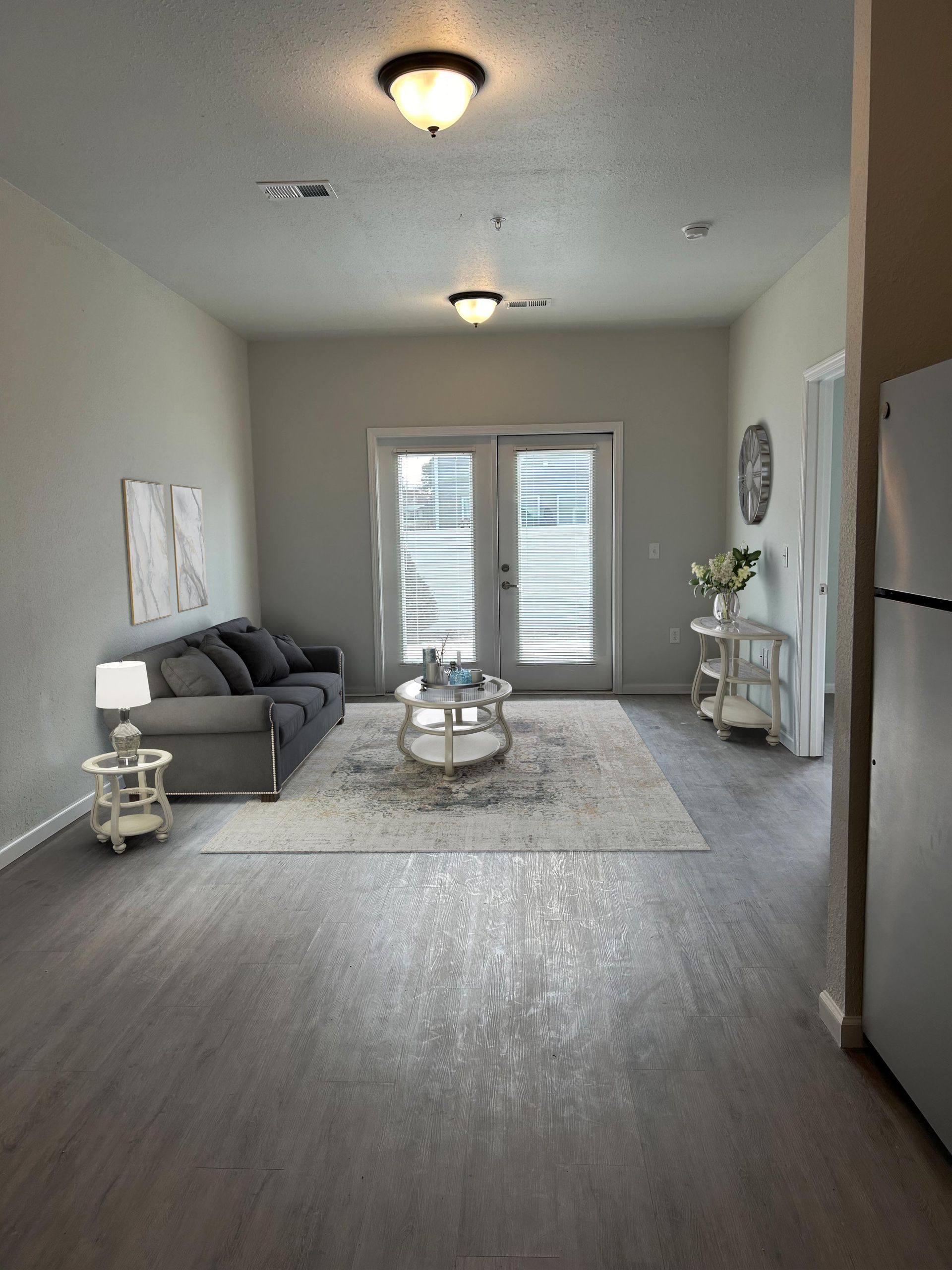 Lincoln, NE, Affordable Apartments - Union at Middle Creek - Living Room With Gray Sofa, Round Coffee Table, Area Rug, And Double Glass Doors With Blinds Leading Outside.