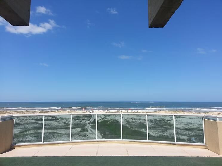 Vista para o mar a partir de uma varanda com guarda-corpo de vidro sob um céu azul límpido