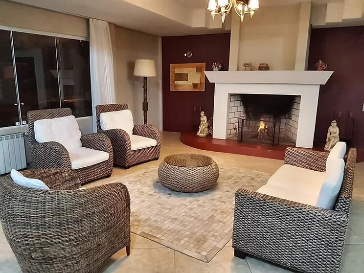 Sala de estar aconchegante, com cadeiras de vime, pufe e lareira branca em uma parede bordô