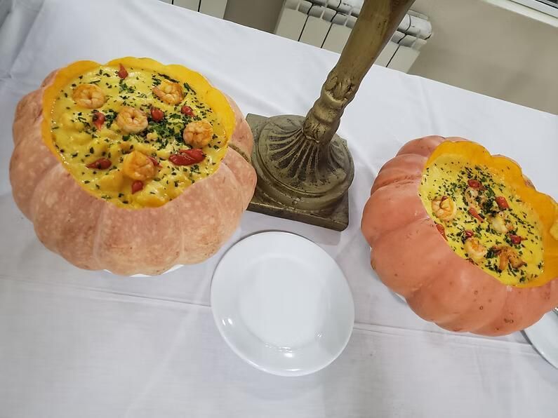 Dois pratos em formato de abóbora com comida amarelo-alaranjada sobre uma mesa branca, ao lado da base de uma luminária de latão