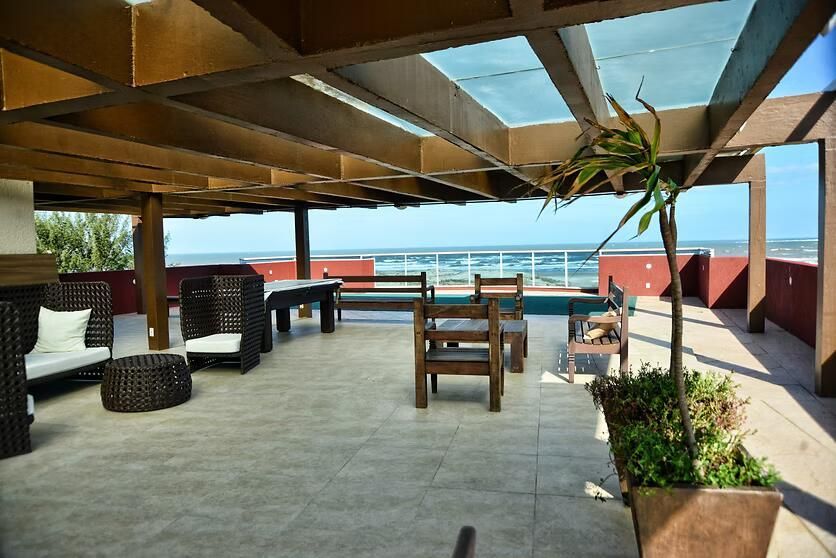 Pátio à beira-mar com móveis de vime, pérgula de madeira e vista para o mar e os telhados