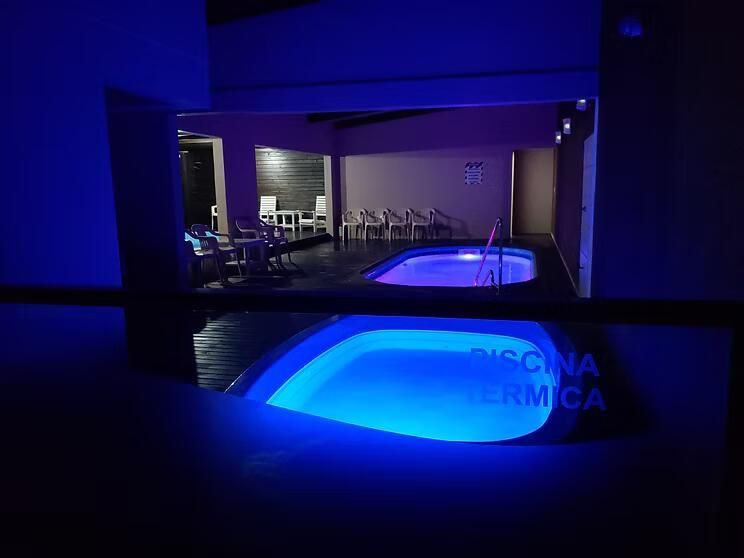 Área de piscina interior iluminada em tons de azul, com um espelho de água e assentos ao fundo