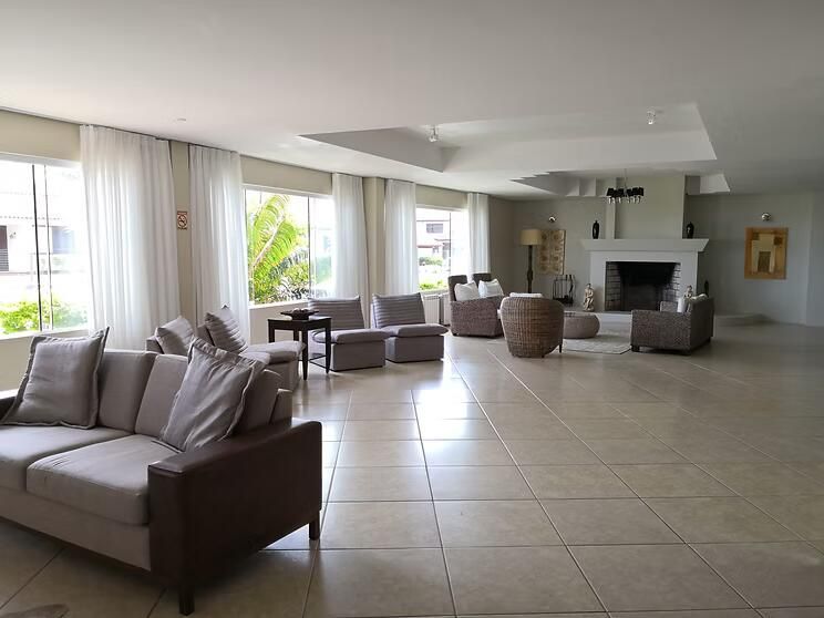 Sala de estar moderna e espaçosa, com sofás, poltronas, piso de ladrilho e janelas amplas com cortinas transparentes