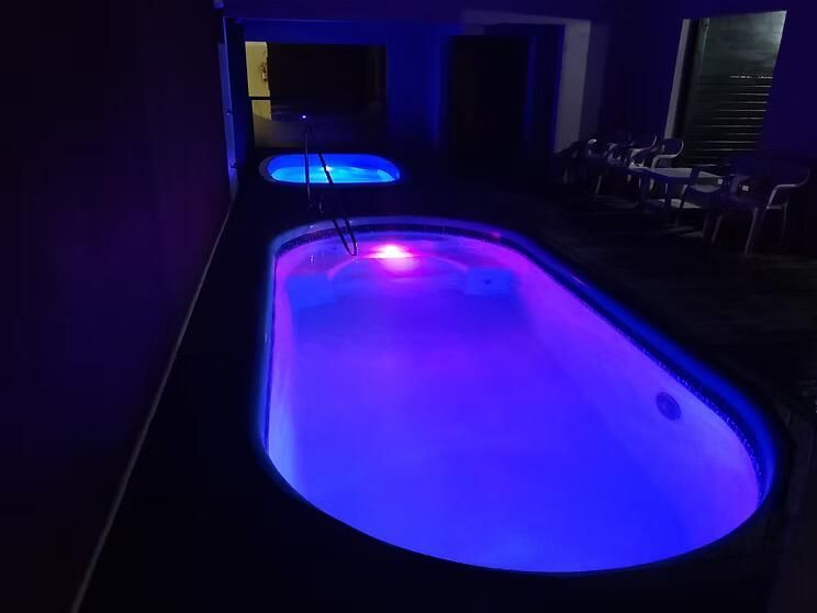Piscina interior iluminada em azul e roxo à noite, com uma piscina menor iluminada ao fundo.