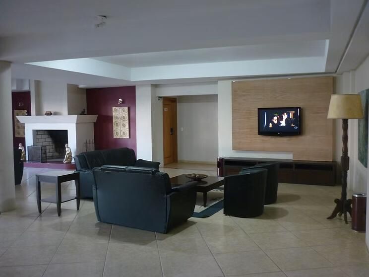 Sala de estar moderna com sofás de couro escuro, piso de ladrilhos, lareira e TV montada na parede