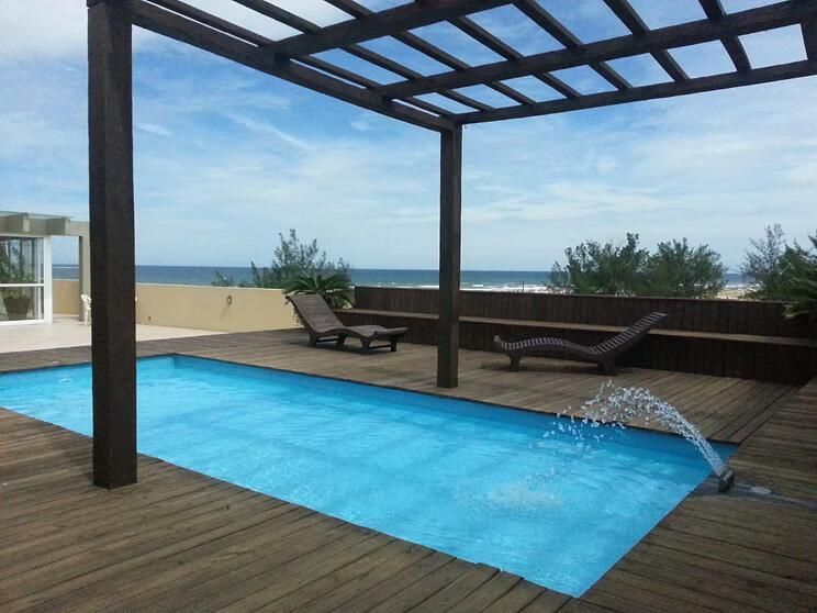 Piscina moderna na cobertura, com água azul, deck de madeira, espreguiçadeiras e vista para o mar