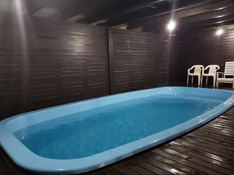 Piscina coberta com revestimento azul em uma sala revestida de madeira escura, com cadeiras brancas em uma das extremidades