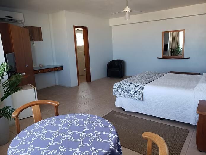 Quarto de hotel luminoso com duas camas, uma cadeira, uma secretária, um espelho e piso de ladrilho