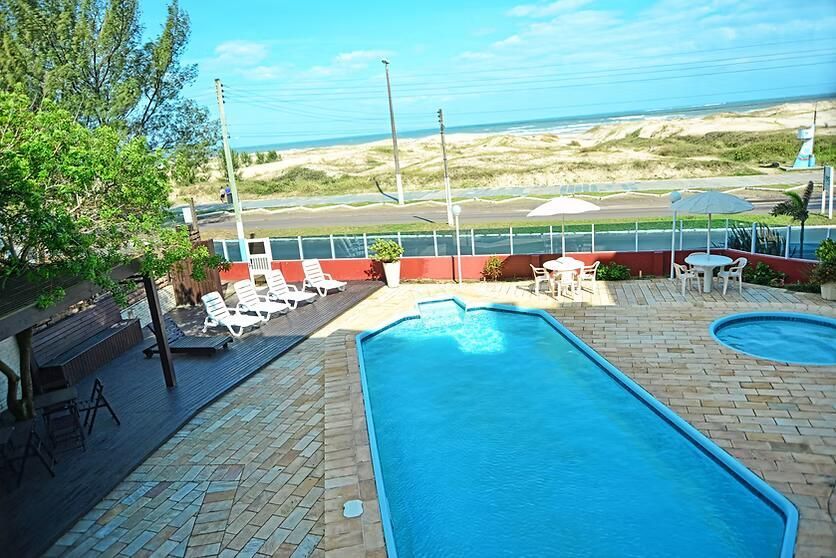 Piscina no quintal com água azul, pátio de pedra, espreguiçadeiras e vista para dunas de areia além da cerca