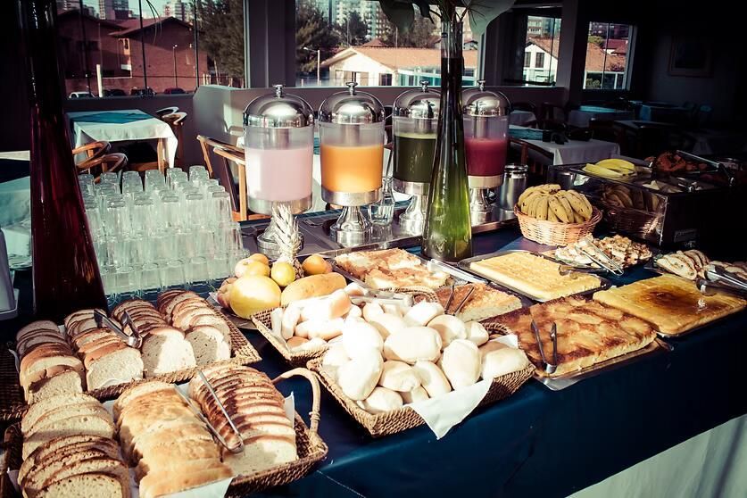 Bufê de café da manhã com doces, pães, frutas e máquinas de café sobre uma mesa