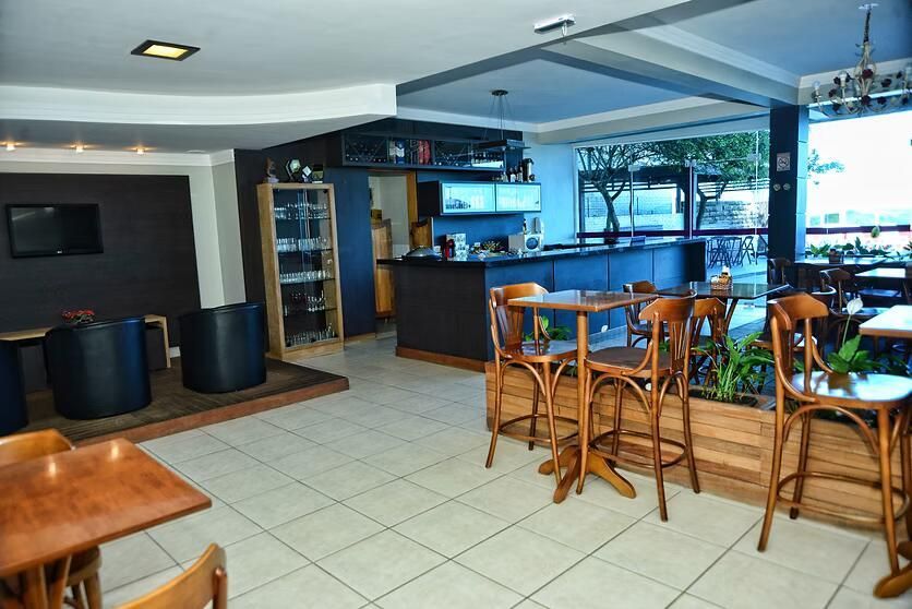 Interior de café vazio com mesas e cadeiras de madeira, piso de ladrilhos e um balcão perto de grandes janelas