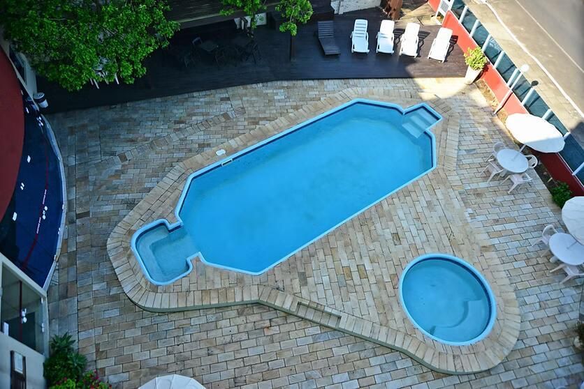 Vista aérea de um quintal com uma grande piscina azul, banheira de hidromassagem e pátio de pedra com espreguiçadeiras.