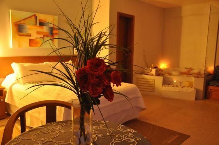 Quarto com iluminação acolhedora, cama, arranjo de flores vermelhas e espelho na parede