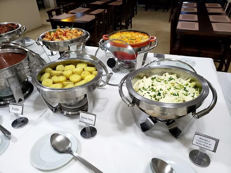 Mesa de buffet com várias travessas de metal com comida numa sala de jantar