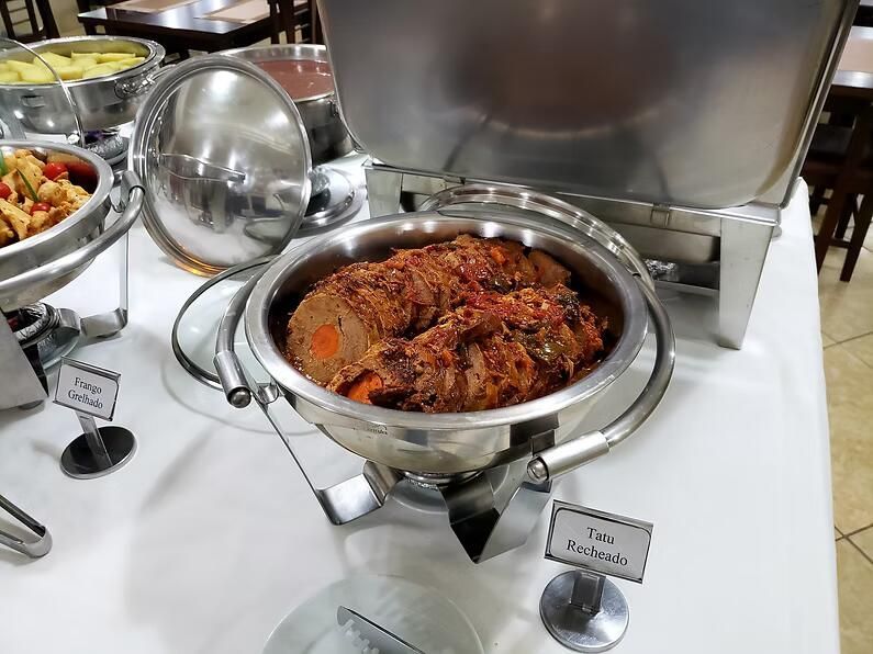 Travessa aquecida de buffet com carne picante castanho-avermelhada, com pinça de servir sobre um balcão de aço inoxidável
