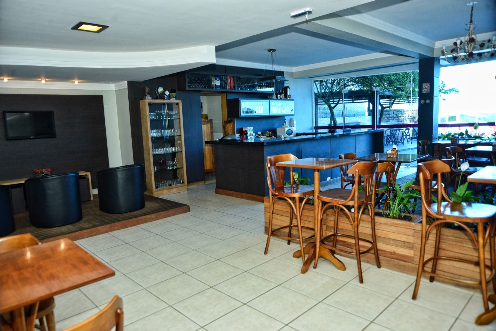 Bar e café ao ar livre, com cadeiras de vime, mesas de madeira e piso de azulejos, com vista para uma área verde
