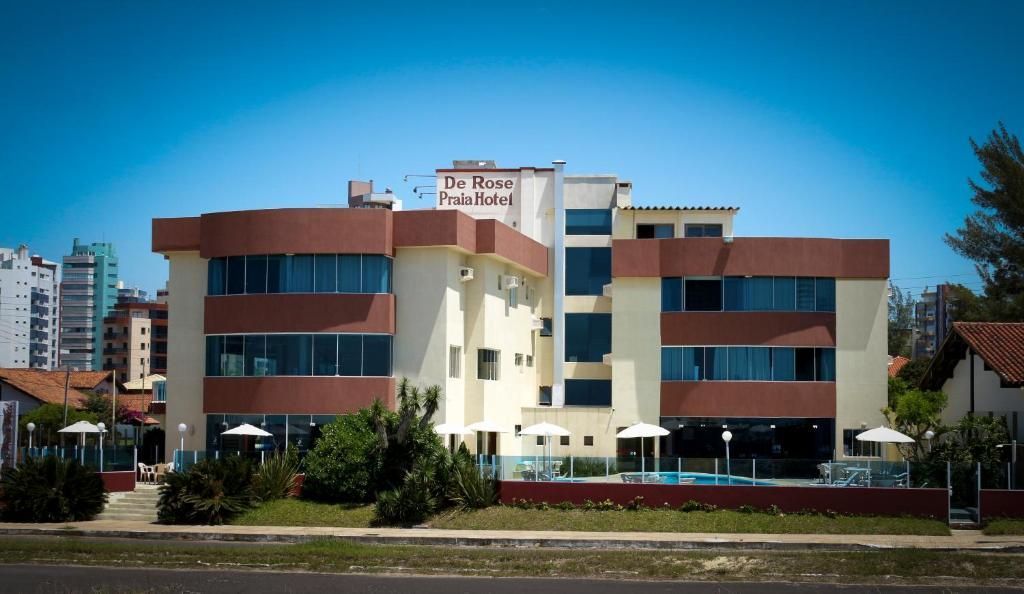 Edifício hospitalar moderno de vários andares, com fachada azul e bege, visto do outro lado de uma estrada sob um céu limpo