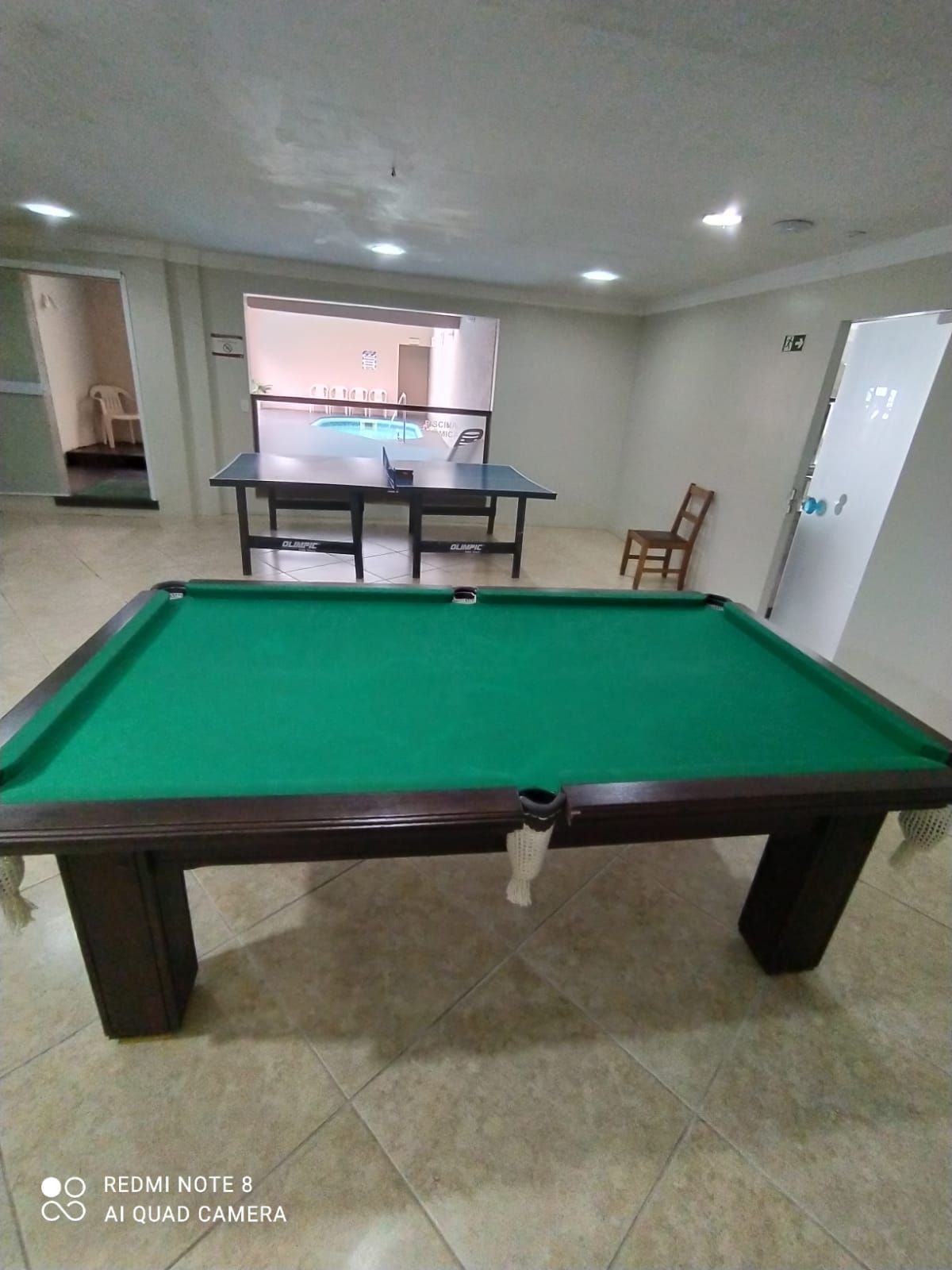 Mesa de bilhar numa sala de jogos bem iluminada, com uma mesa de jantar e cadeiras ao fundo.