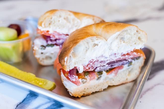 Bagel sandwich with cream cheese, deli meat, and vegetables on a metal tray