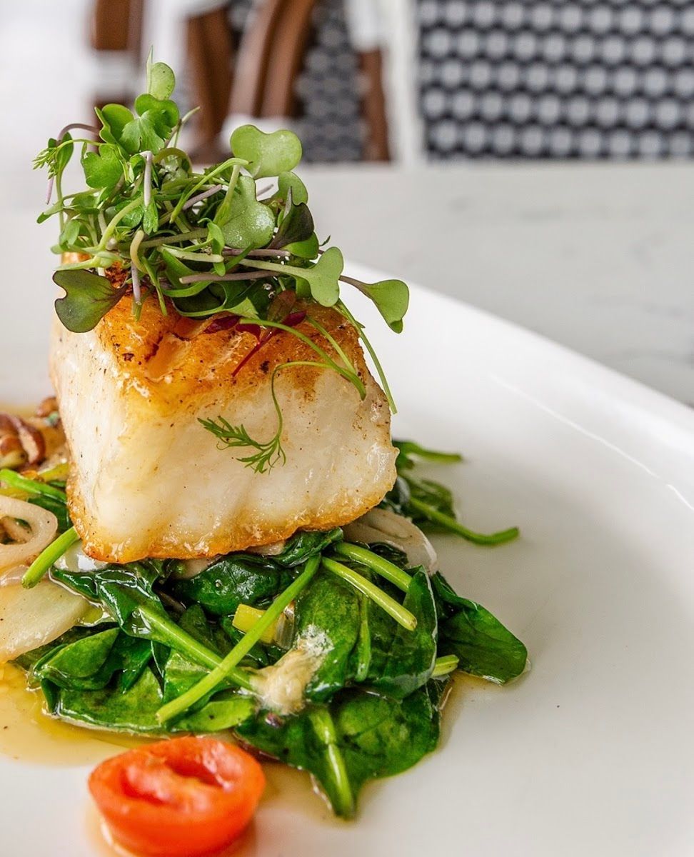 Seared white fish on sautéed greens with microgreens and cherry tomato on a white plate