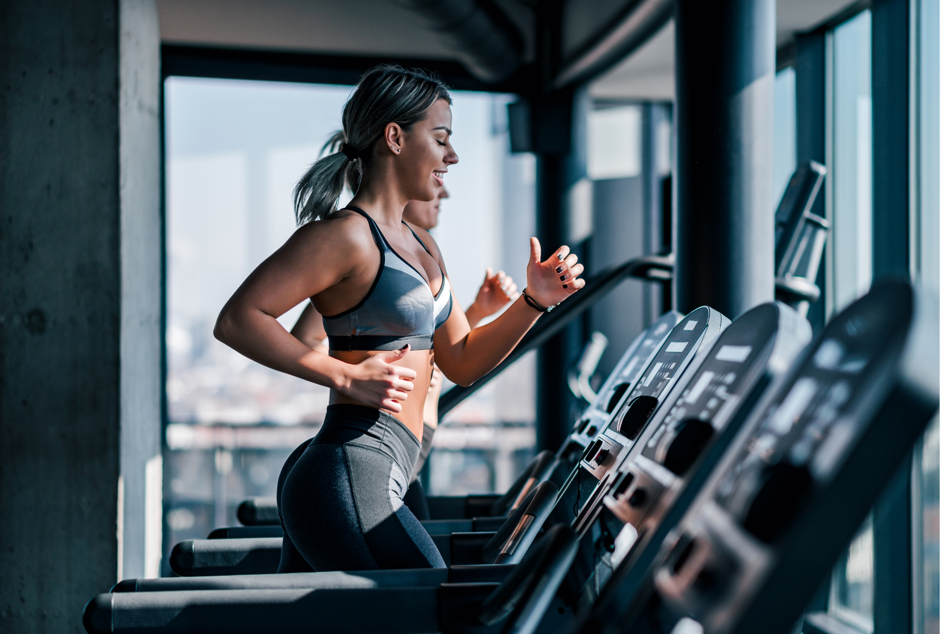 Woman running on a treadmill in a gym, focused on a row of cardio machines.