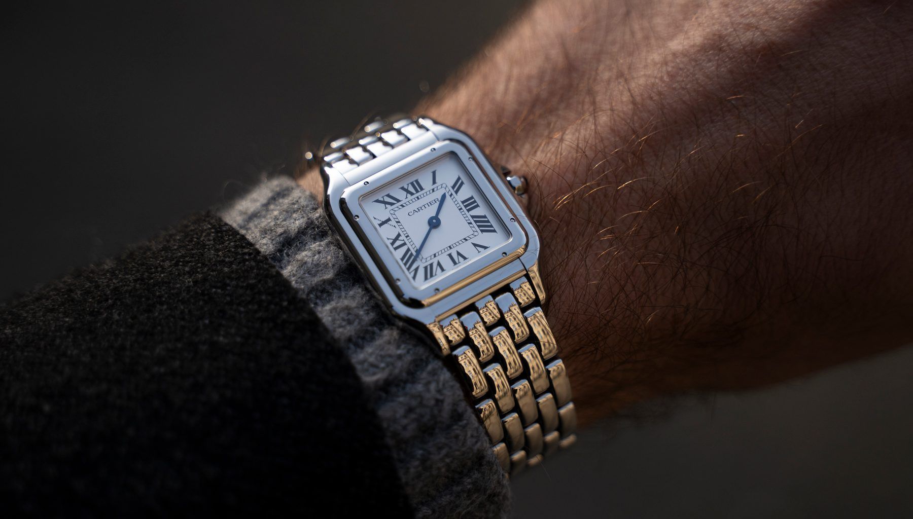 Close-up of a silver rectangular wristwatch with gold accents on a person’s wrist.