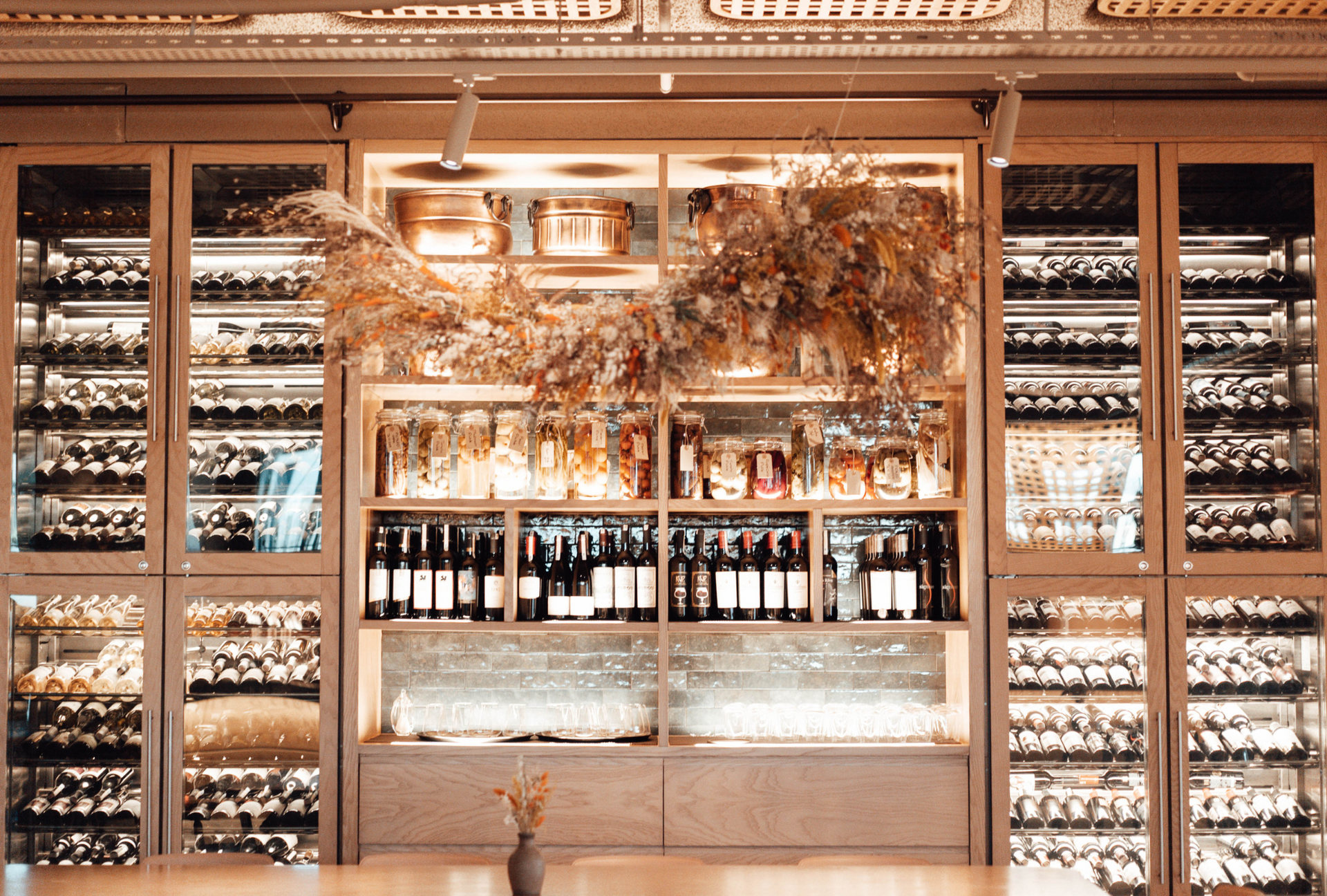 Elegant wine bar with shelves of bottles and glasses behind a central counter, lit warmly in gold tones