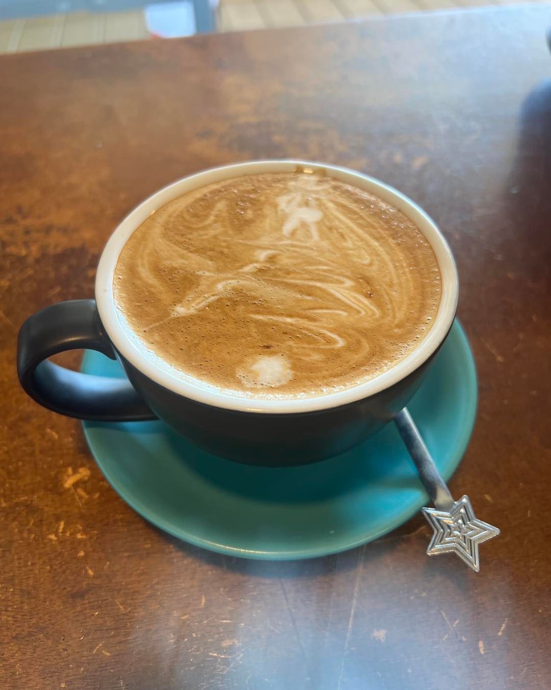 Cup of Coffee With Latte Art on a Teal Saucer and Star Spoon — Memories Cafe @ Yorkeys Knob in Yorkeys Knob, QLD
