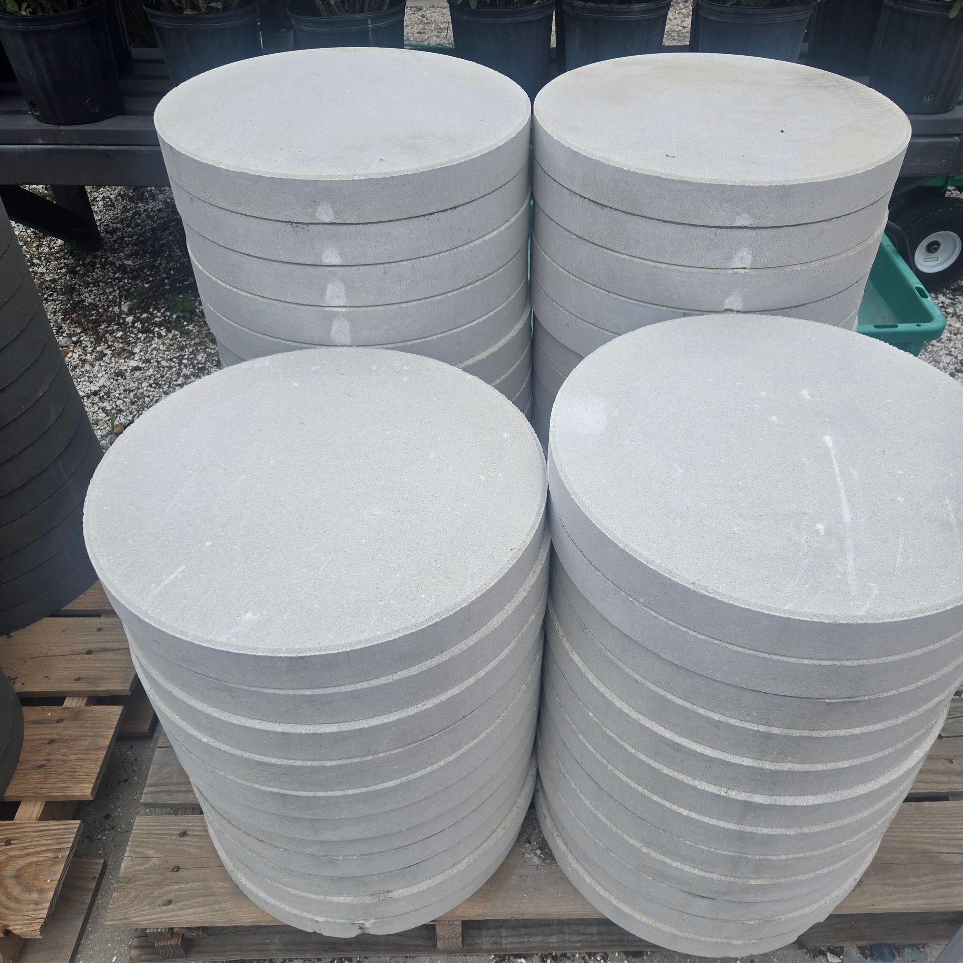 Stacks of round white concrete pavers or lids arranged outdoors on a pallet and gravel.