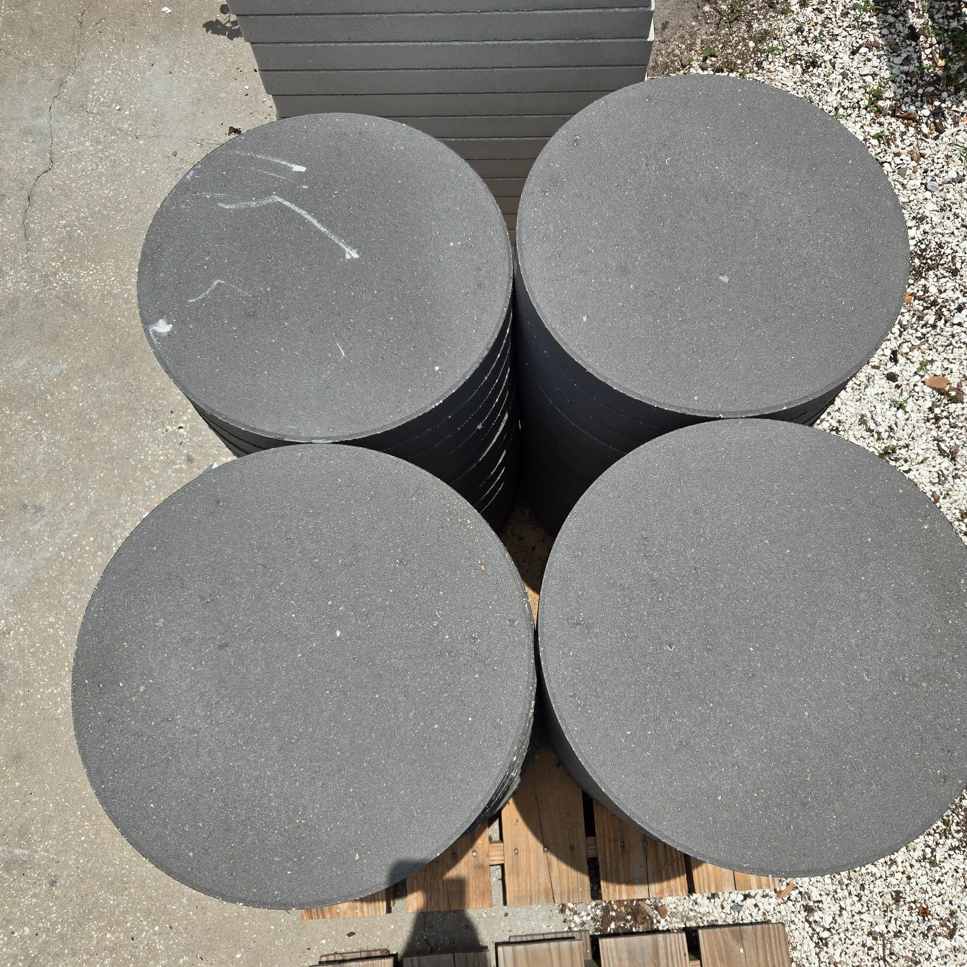 Four gray cylindrical foam rolls stacked on a wooden pallet outdoors on concrete and gravel.