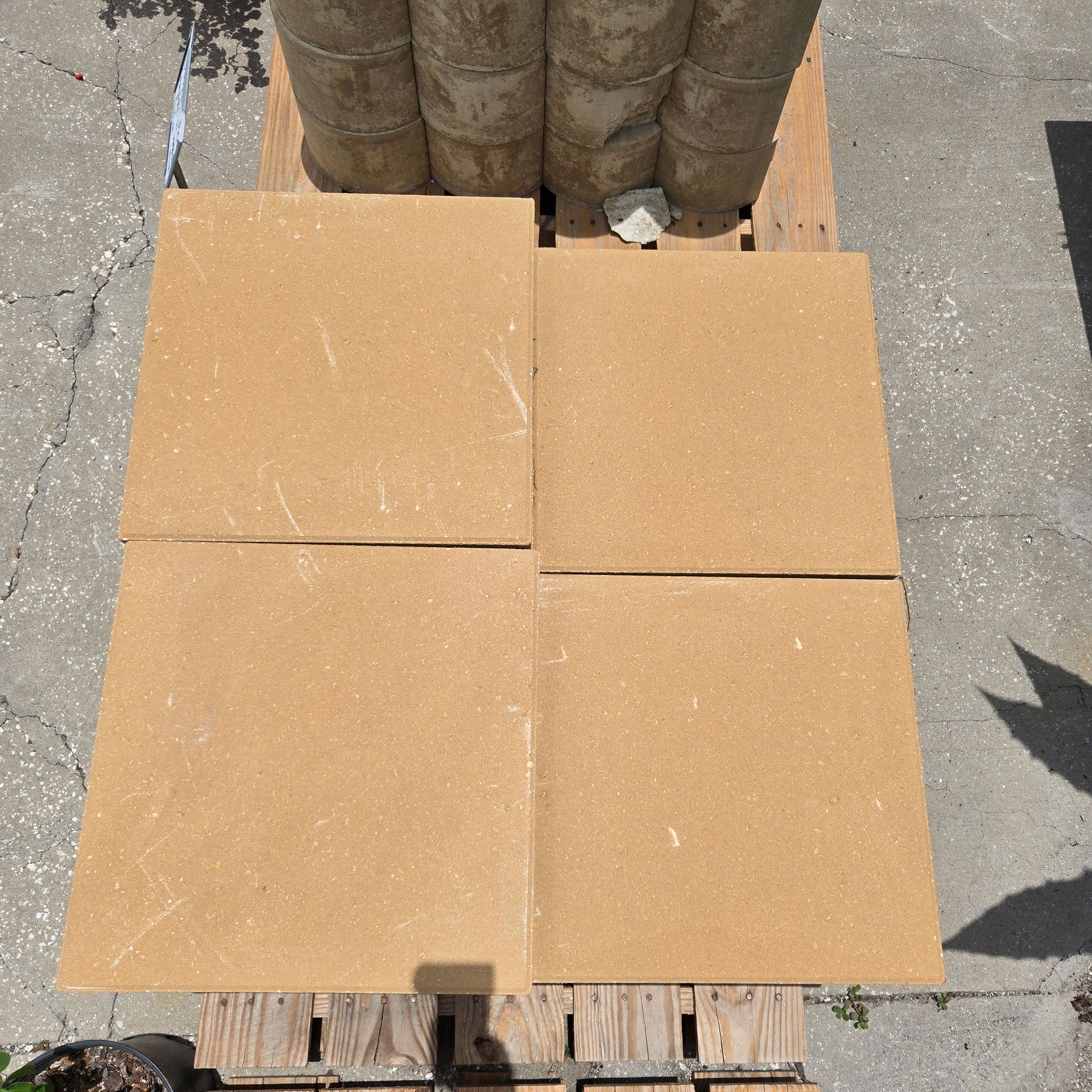 Four cardboard sheets arranged on a wooden pallet outdoors beside bundled rolls.