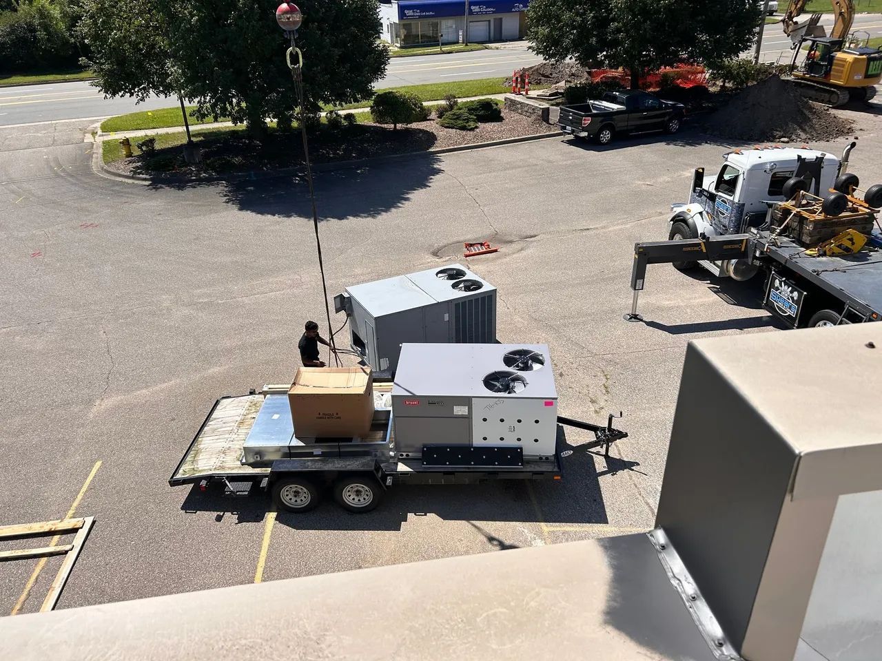 A crane lifting an HVAC unit off a trailer at a construction site.