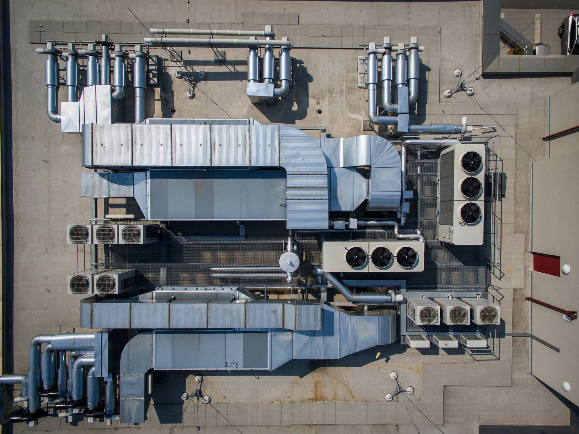 Top-down aerial view of industrial HVAC rooftop equipment with ductwork and cooling units on a flat concrete surface.