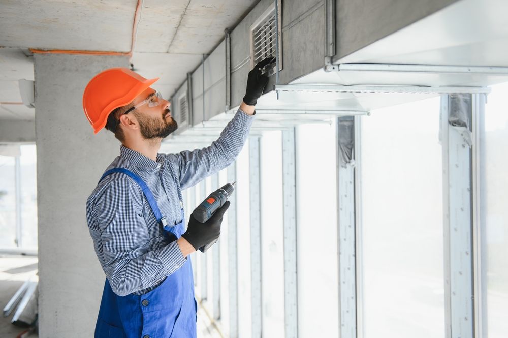 HVAC technician in orange hard hat examines ductwork in a building under construction.