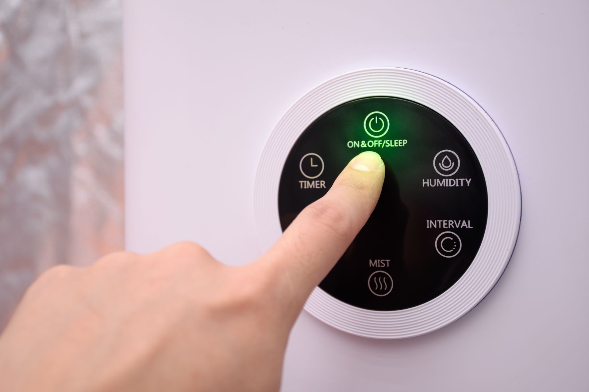 Finger pressing a circular touch control panel with green-lit power icon and labels on a white appliance