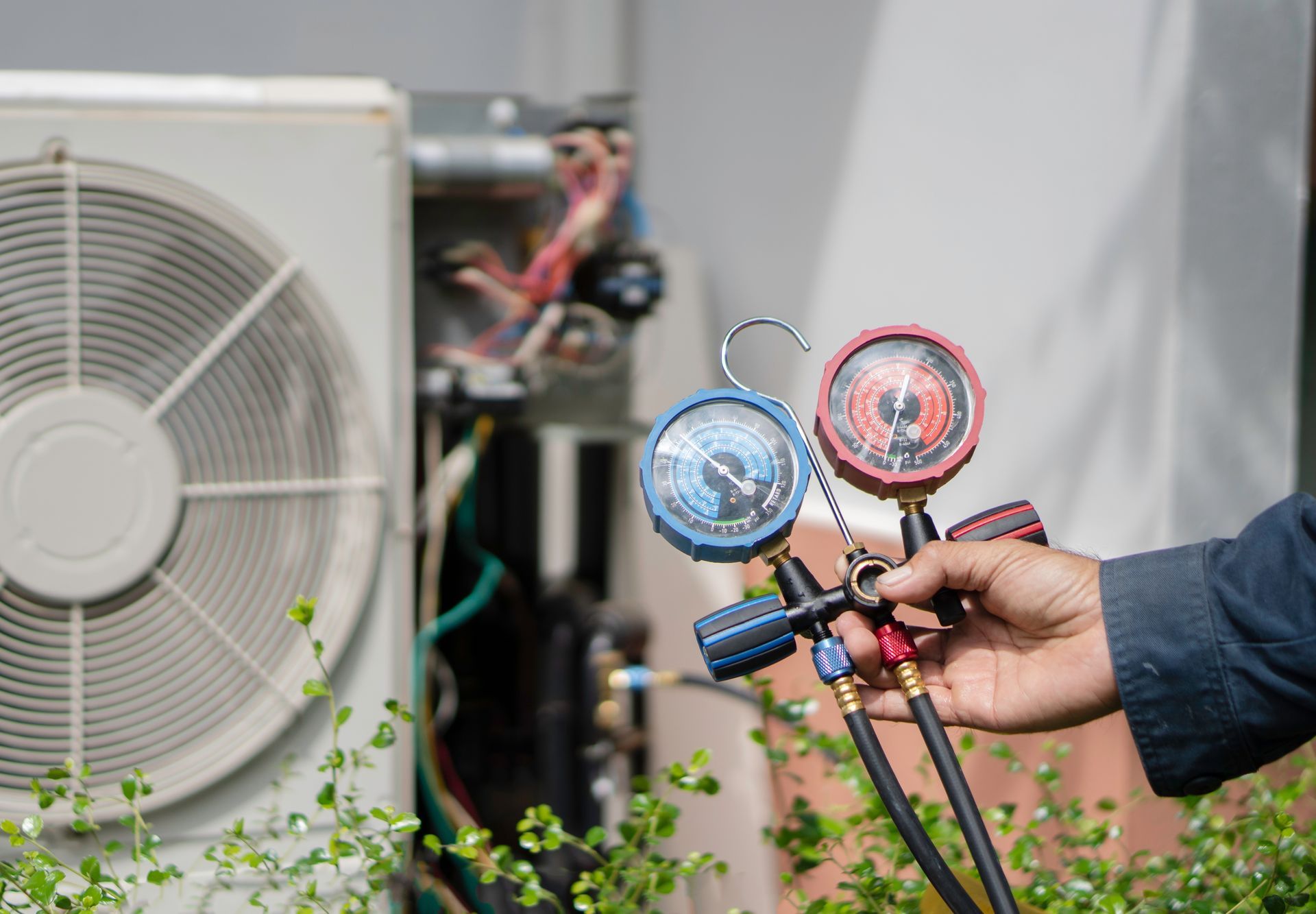 Person holding gauges near an air conditioner unit, testing pressure.