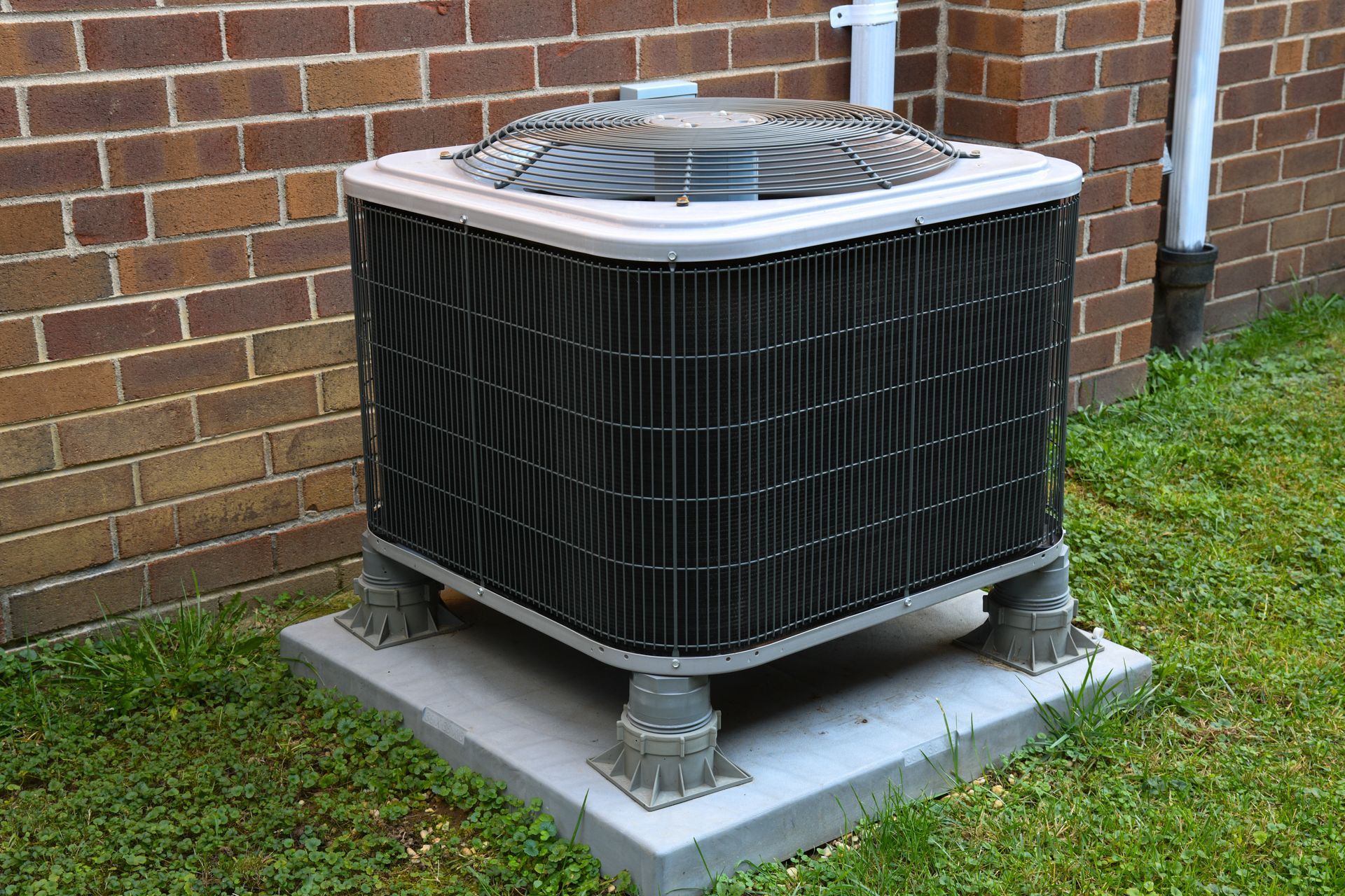 Gray air conditioning unit outside a building with green shrubbery.