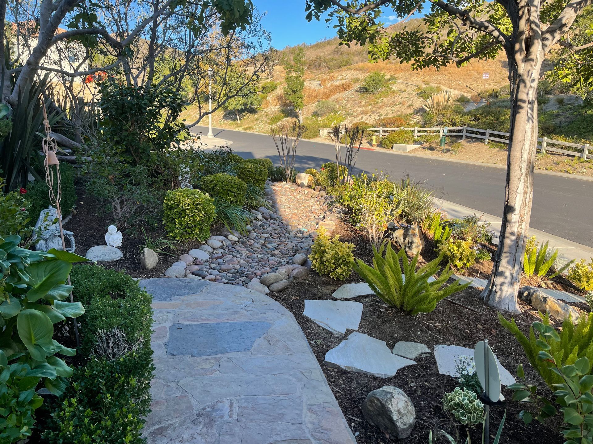 A stone walkway leading to a road surrounded by trees and bushes.