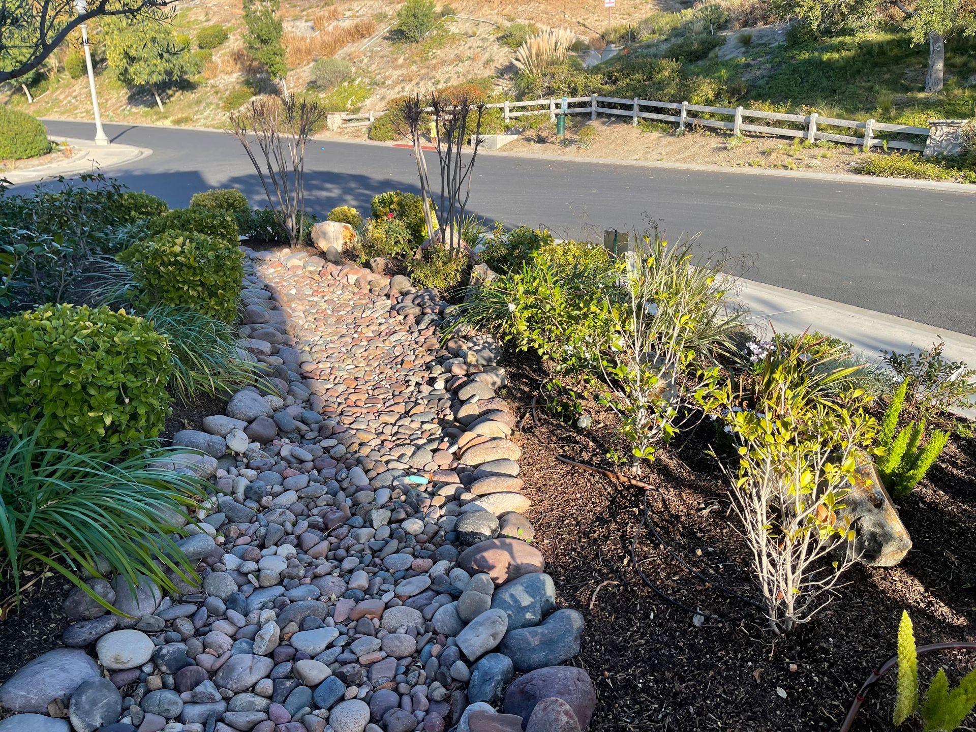 A rocky path leading to a road with a fence in the background.
